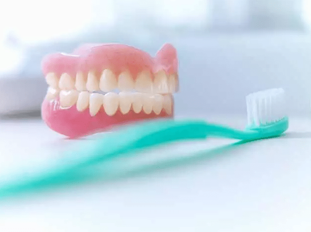 A set of dentures next to a turquoise tooth brush