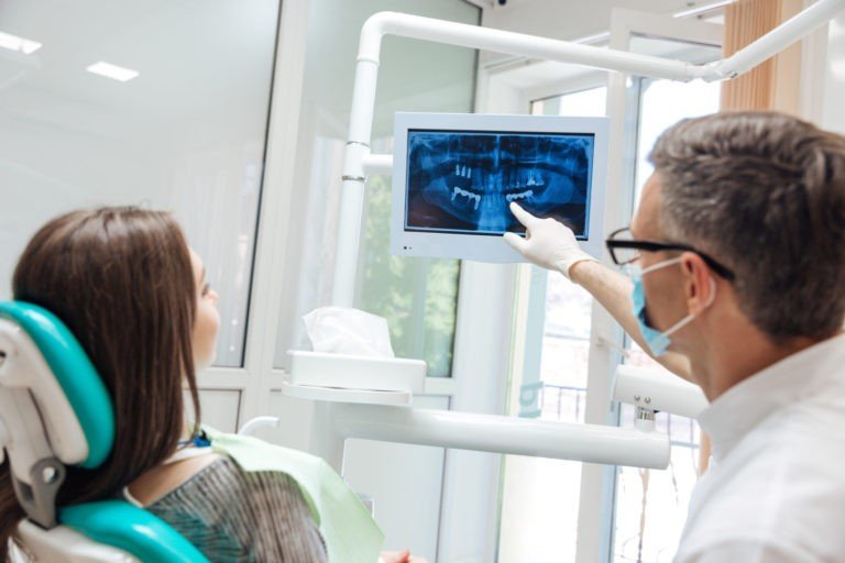 A dentist points at a digital monitor with an x-ray, for a patient